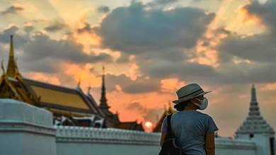 سائحة ترتدي قناعاً للوقاية من فيروس كورونا أثناء غروب الشمس بالقرب من القصر الكبير في بانكوك عاصمة تايلندا